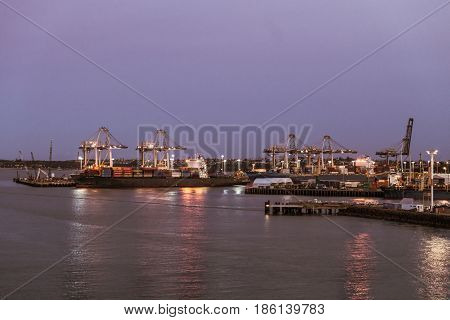 Auckland New Zealand - March 6 2017: Overview of the container terminal at sunset with ships. Lights on the docks reflected in the water.