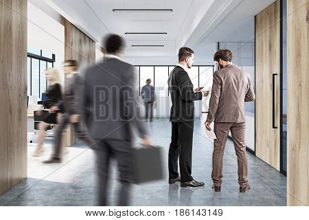 Company employees in a white open office interior with panoramic windows wooden walls computer monitors on desks and a reception counter in the lobby. 3d rendering