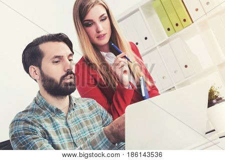 Portrait of a bearded young man in a checkered shirt showing his data on a laptop screen to a beautiful colleague standing near him. Toned image.