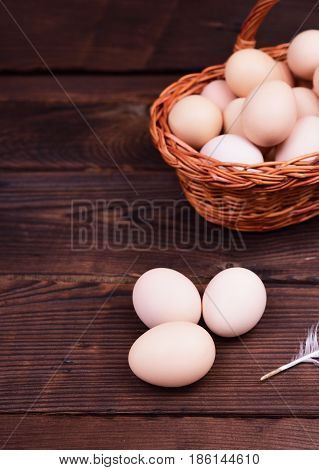 Fresh chicken eggs on a brown wooden surface behind a full wicker basket of eggs