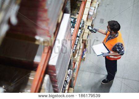 Worker with scanner making review of goods in warehouse