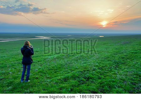 Woman hiker standing in the meadow with blossoming flowers in spring and watching sunrise. New day expectations. New hopes