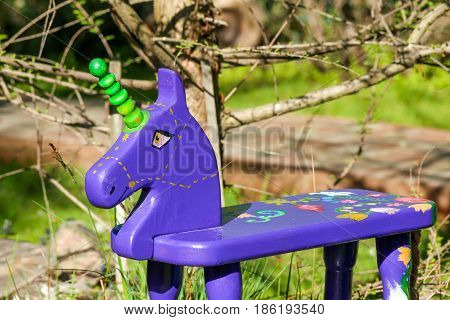 A handmade violet rocker horse toy standing in a garden.