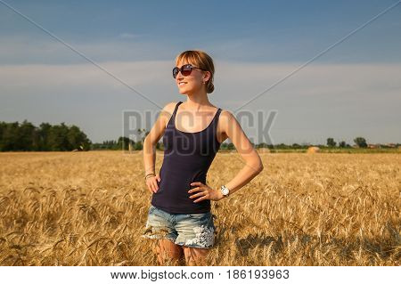 A young beautiful woman standing at wheat field under sunlight.