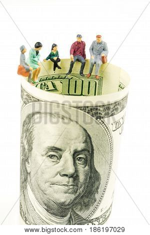 miniature figurines sitting on the edge of 100 dollar banknote on white background