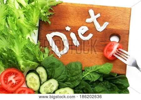 Various vegetables Lettuce frize spinach tomatoes cucumbers beautifully laid out near the cutting board with the word diet written cheese mascarpone sour cream. On the board is a fork with a slice of tomato. Symbol of diet lacto vegetarianism and healthy