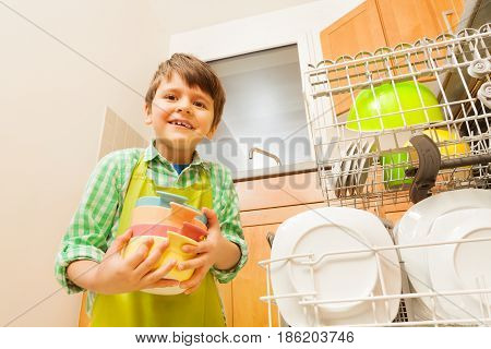 Portrait of six years old boy loading dirty dishes to dishwashing machine