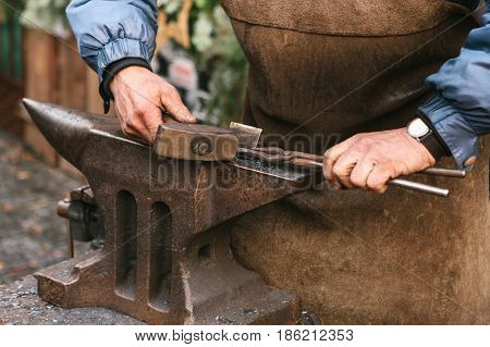 Blacksmith working metal with a hammer on the anvil in the forge. Outdoors scene.