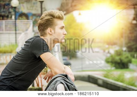 Profile shot of attractive blond young man in city, looking away in the distance, outdoor