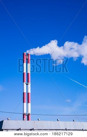 Two striped pipes smoke against a blue sky vertical