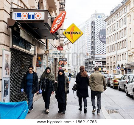STRASBOURG FRANCE - MAY 7 2017: Three muslims girls walking on trottoir under Loto and press signage in French city of Strasbourg