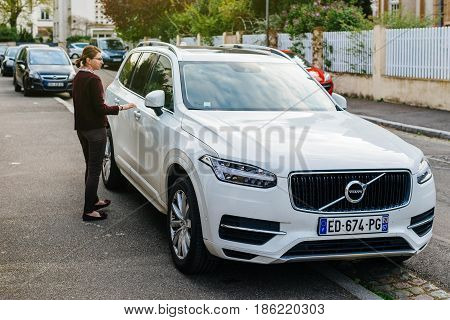 PARIS FRANCE - APR 2 2017: French woman aproaching her luxury white Volvo XC90 the luxury crossover SUV manufactured and marketed by Volvo Cars