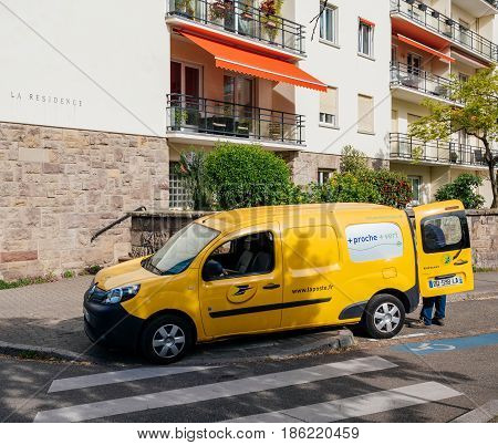 STRASBOURG FRANCE - APR 12 2017: Yellow van of La Poste - French National Postal service with postal driver worker searching gor the right parcel to deliver near French building