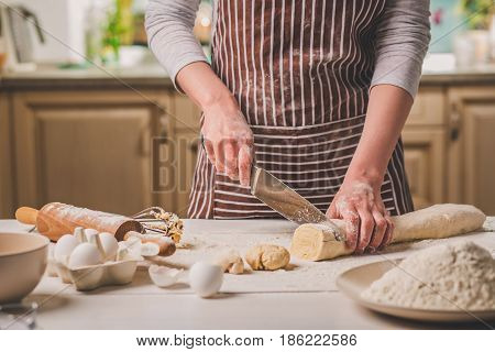 Close-up view of two woman's hands cut knife dough. A woman in a striped apron is cooking in the kitchen