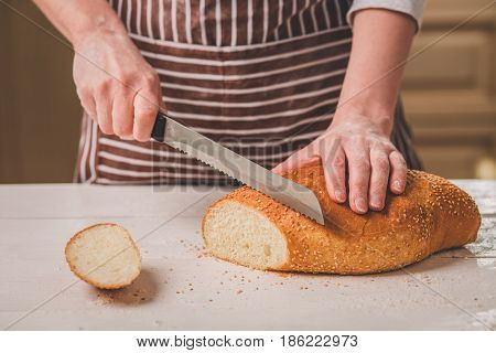 Woman cutting bread on wooden board. Bakehouse. Bread production. A woman in a striped apron