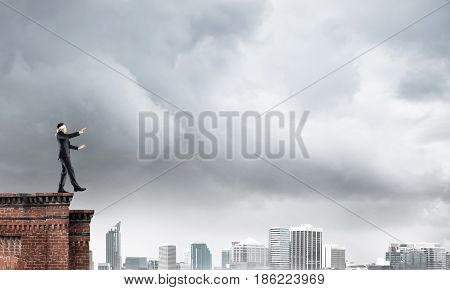 Businessman with blindfolder on eyes walking on building top