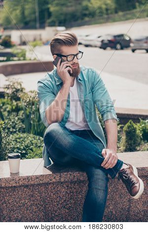 Stylish Young Red Bearded Man In Casual Jeans Outfit Is Talking On His Phone Outside. He Looks Fashi