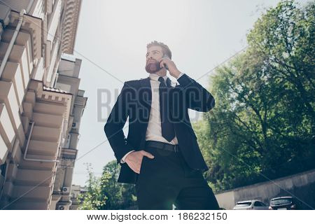 Low Angle View Of A Young Handsome Bearded Business Man In A Classy Suit Talking On His Mobile Outdo