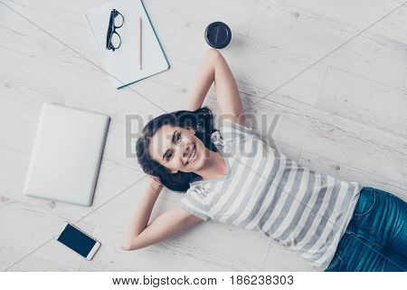Top View Of Girl Resting On The Floor And Smiling. She Is Happy, Her Hands Are Behind The Head, She