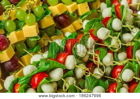 appetizer canape cheese with white and red grapes and tomato on bamboo skewers