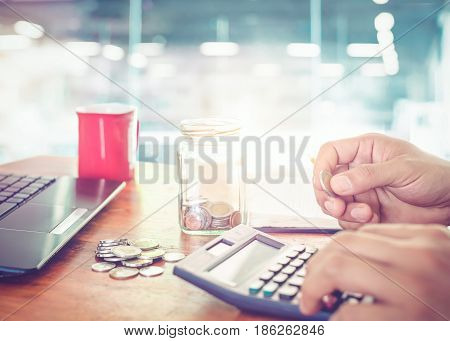 young businessman using calculator for finance tax and saving money. Business man working at modern business office and take a coin for count money. Vintage color filter.