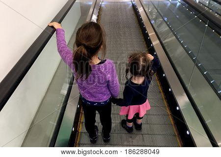 Two sister holds hands on moving walkway. Real people. copy space