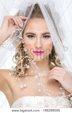 Beautiful young woman in wedding gown with make-up and mask drawn around eyes. Bride with big white bow on head.  Beauty closeup shot.