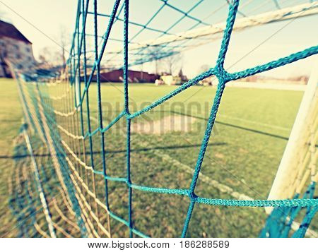 Detail of yellow blue crossed soccer nets soccer football in goal net with grass on outdoor playground in the background.