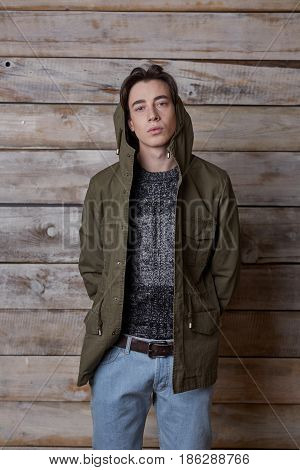 Handsome man wearing green jaket and torn jeans in wooden rural house interior
