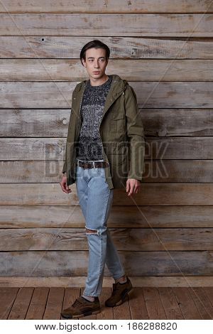 Handsome man wearing green jaket and torn jeans in wooden rural house interior