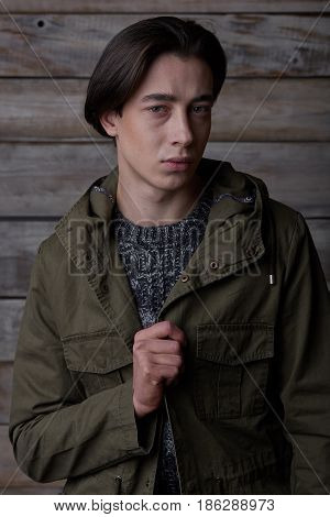 Handsome man wearing green jaket and torn jeans in wooden rural house interior