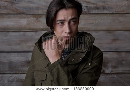 Handsome man wearing green jaket and torn jeans in wooden rural house interior