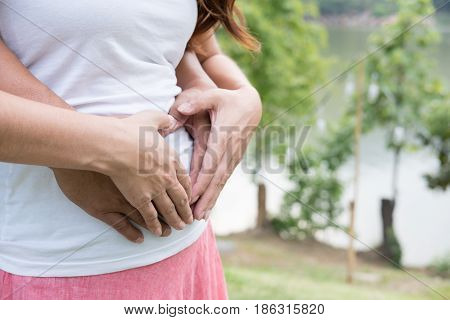 Young Asian Woman And Her Husband Together Caressing Her Pregnant Belly Holding Their Hands In A Hea