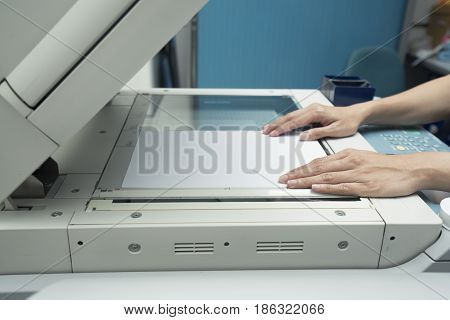woman hands putting a sheet of paper into a copying device