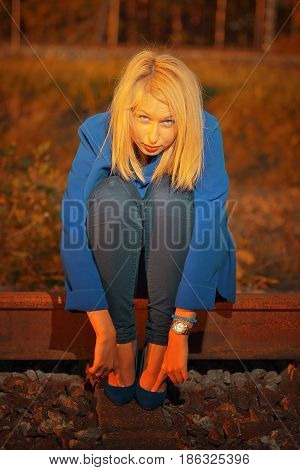 blond woman in blue coat posing on railraod on sunset time