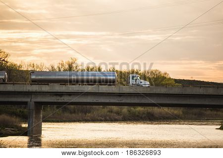 Semi truck with tanker trailers driving on a bridge over a river.