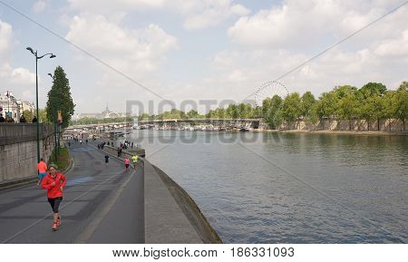ParisFrance- April 292017:Athletes run along the Port de Solferino.People walk around.In the foreground runs a lady in a red suit