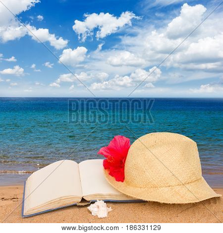 straw hat and book on beach sand by sea side