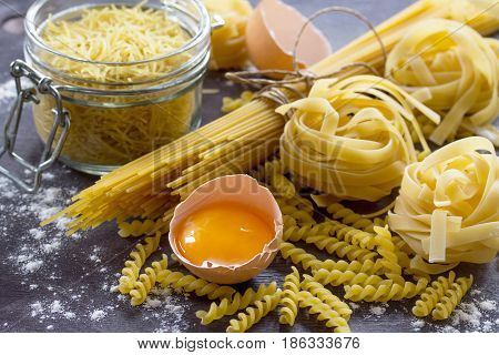 Different Kinds Of Pasta Spaghetti, Fusilli, Fettuccine And Raw Egg Yolk On The Kitchen Wooden Table