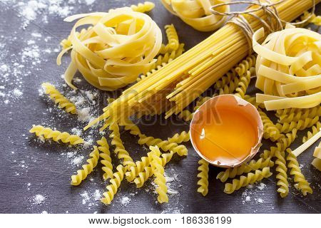 Various Types Of Pasta Spaghetti, Fusilli, Fettuccine And Raw Egg Yolk On A Kitchen Wooden Table. Co