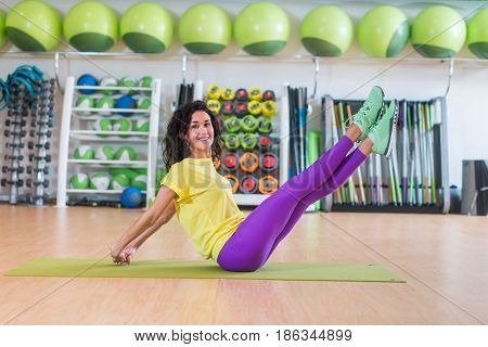 Pretty fitness model doing scissors exercise sitting on floor crossing and uncrossing straight legs smiling and looking at camera.