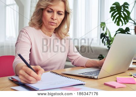 Close-up of pokerfaced woman writing while working in laptop