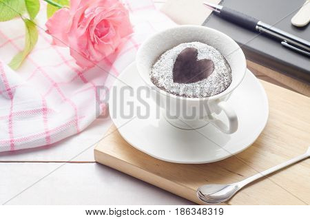 Notebooks pen and chocolate cake in a cup with rose flower on white wooden background. flower on white wooden background.
