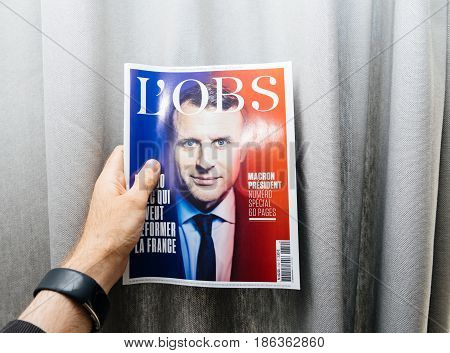 PARIS FRANCE - MAY 10 2017: Man holding L'Obs newspaper front page against gray background with the picture of the newly elected French president Emmanuel Macron the 8th President of France