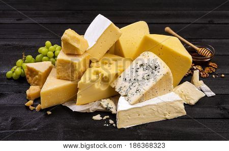 Various types of cheese on black wooden table background. Cheddar, parmesan, emmental, blu cheese.