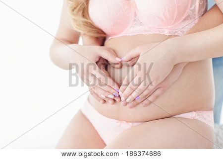 Belly of a pregnant woman Hands hold a heart