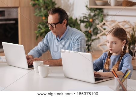 Do not care about world around . Senior retired incurious man sitting at home and using laptops with granddaughter while playing games and checking social media profiles
