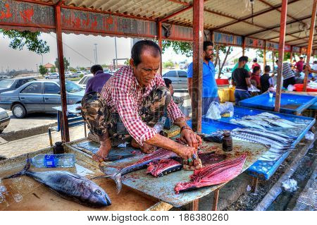 Bandar Abbas Hormozgan Province Iran - 16 april 2017: The seller of fish in the outdoors fish market squatting under a canopy and cuts fresh tuna