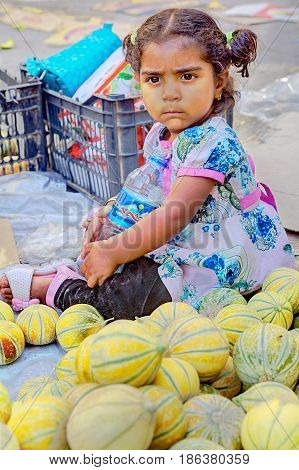Bandar Abbas Hormozgan Province Iran - 16 april 2017: One unknown little girl about three years old sits outside the eastern bazaar on the sidewalk near the melons just editorial use.