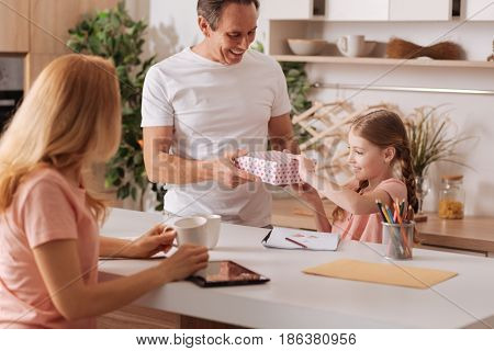 Time or celebration. Smiling caring loving parents enjoying holiday at home and relaxing while giving gift box to the kid